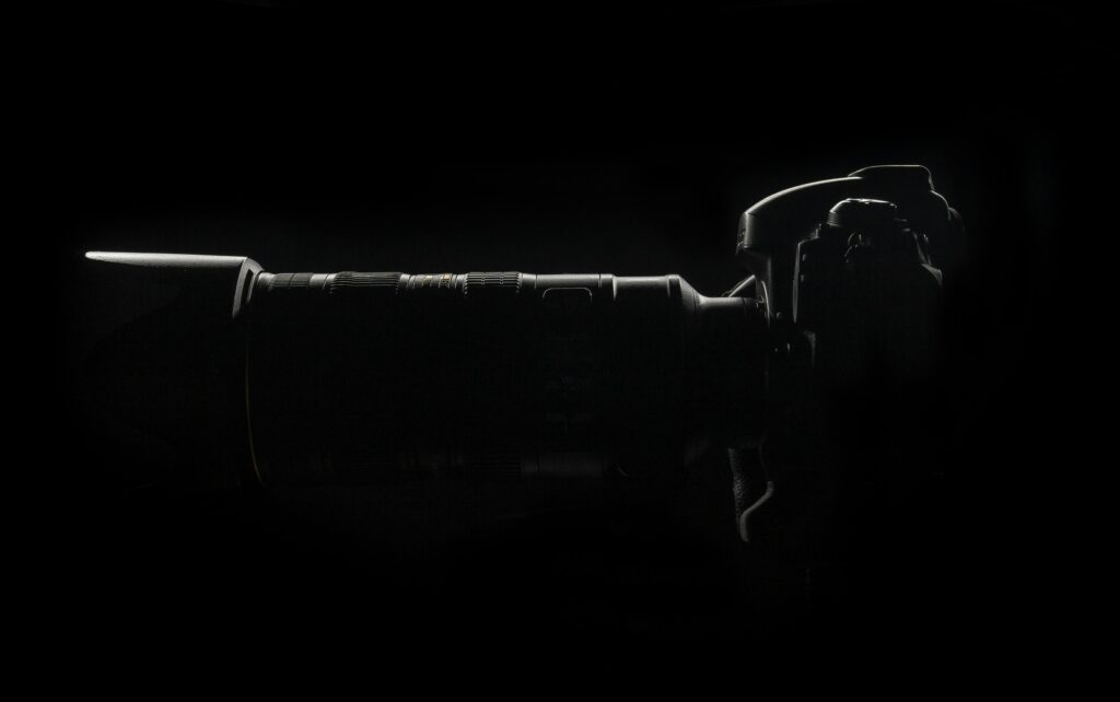 Moody silhouette of DSLR camera with attached lens against dark background.